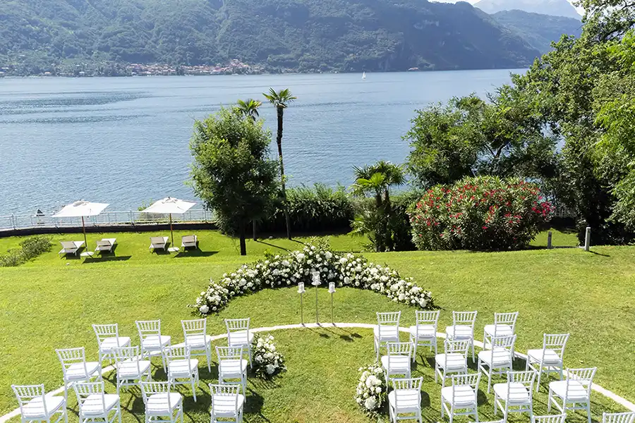 Outdoor wedding ceremony setup on Lake Como with white chairs, floral arch and panoramic lake view.