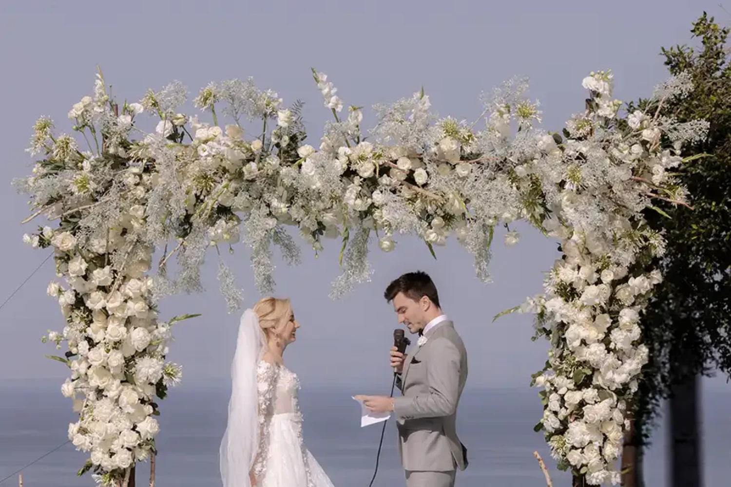 Bride and groom exchanging vows beneath a white floral arch with sea view in Sicily