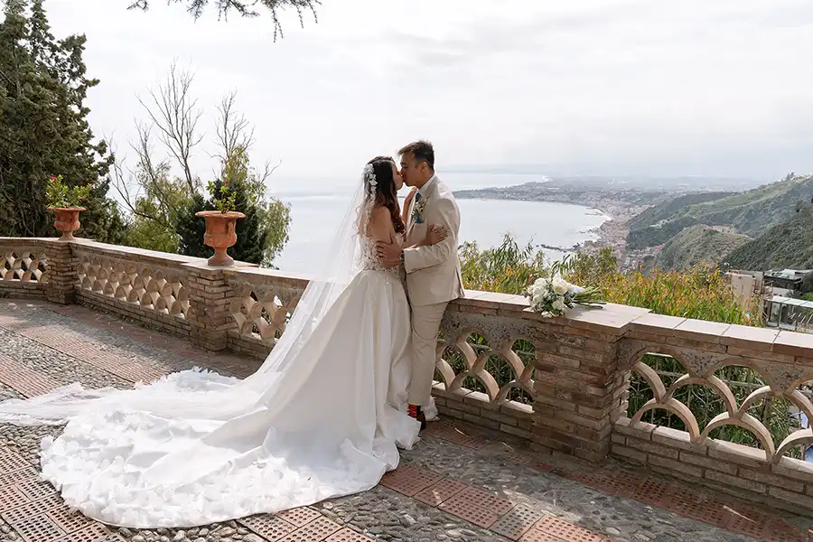 Bride and groom kissing on a panoramic terrace overlooking the Sicilian coast