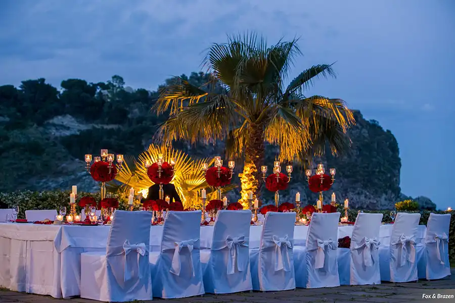 Romantic evening wedding reception in Sicily with red floral centrepieces and candlelight