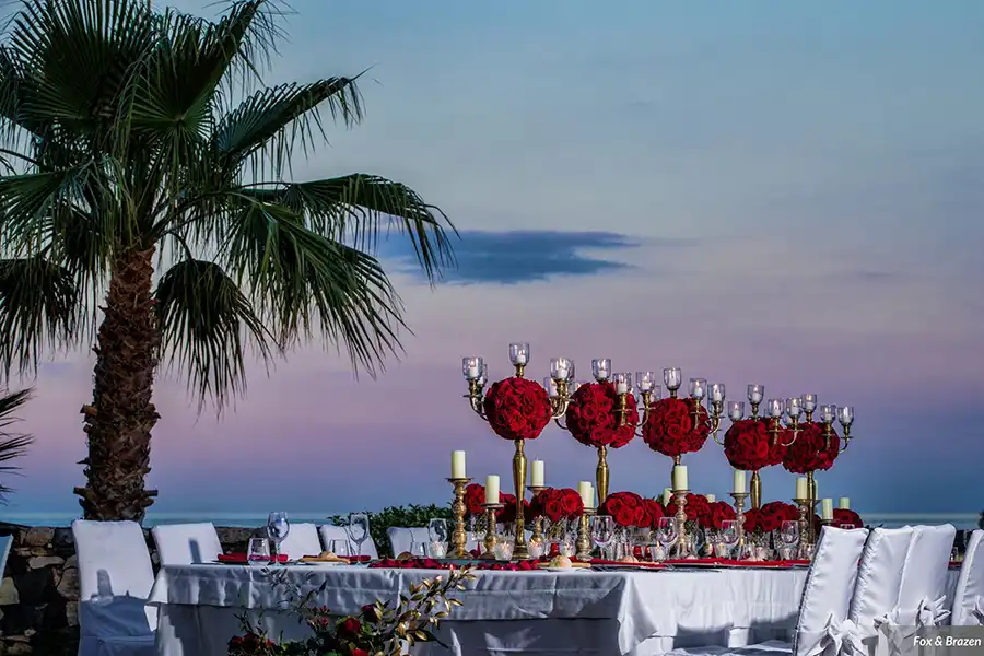 Evening wedding reception table in Sicily with red centrepieces and sea view at dusk
