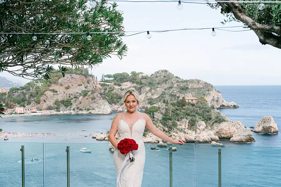 Bride with red bouquet on a panoramic terrace overlooking the sea in Taormina