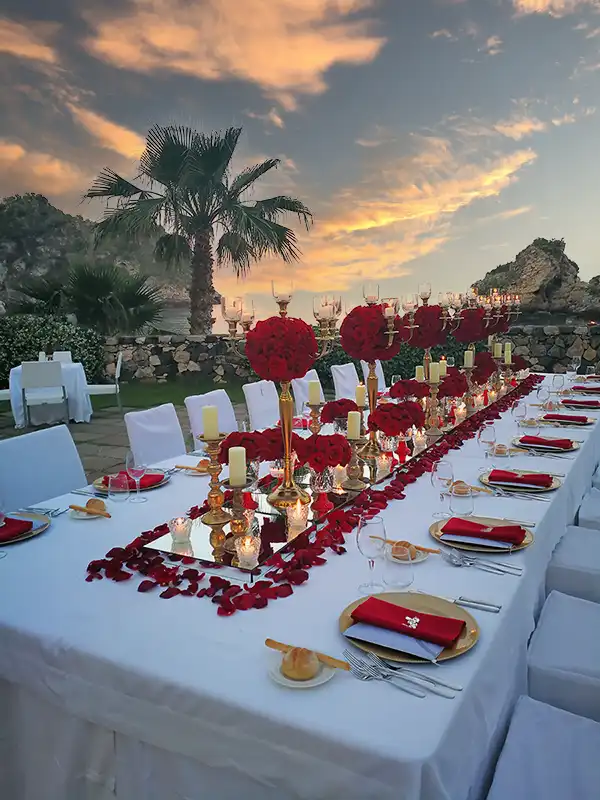 Luxury wedding table in Sicily with red floral centrepieces overlooking the sea at sunset
