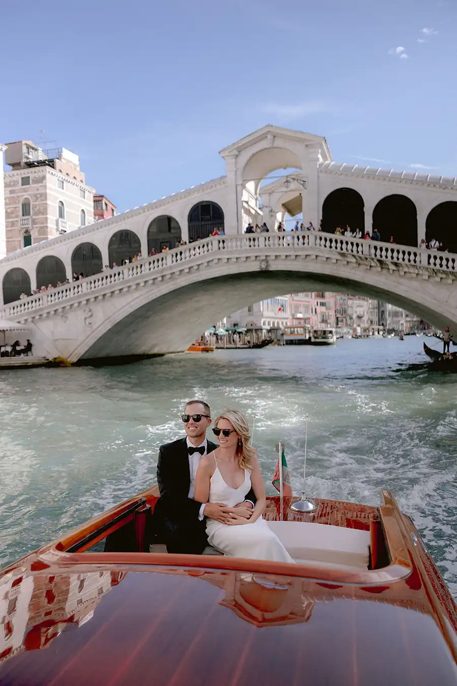 Bride and groom on a classic wooden water taxi near the Rialto Bridge during a wedding in Venice