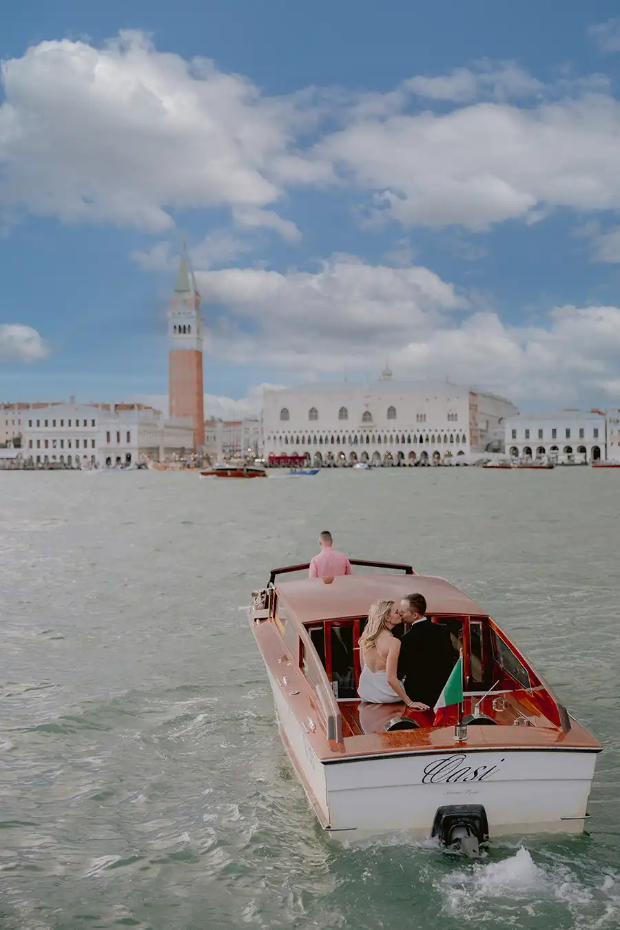 Bride and groom on a wooden water taxi with views of Piazza San Marco and the Doge’s Palace during a wedding in Venice