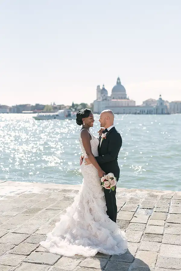 Bride and groom by the waterfront with Santa Maria della Salute in the background during a wedding in Venice