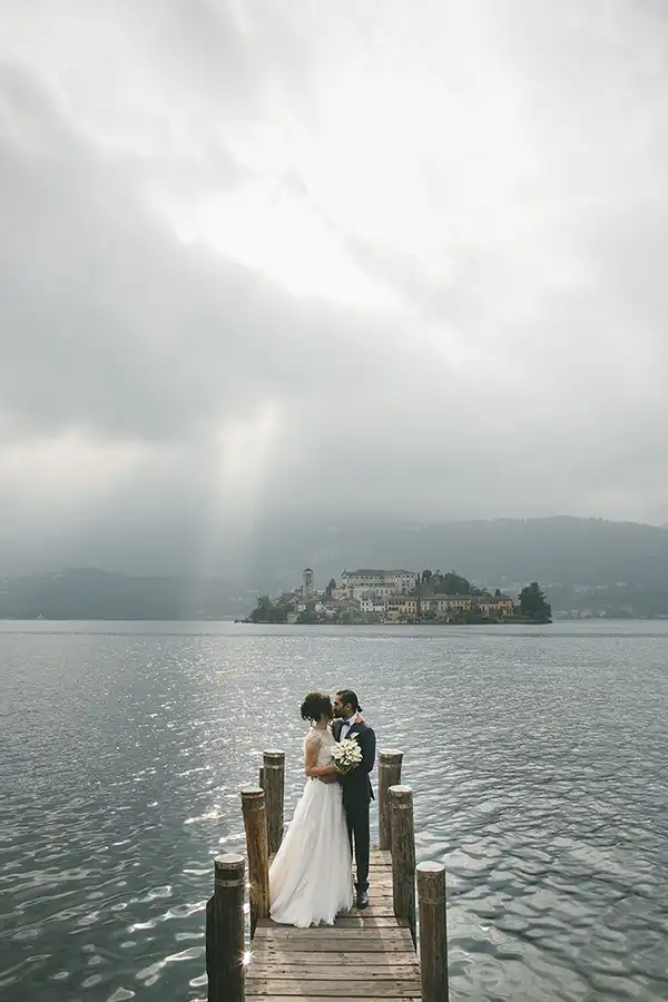 Bride and groom on a lakeside pier overlooking San Giulio Island on Lake Orta